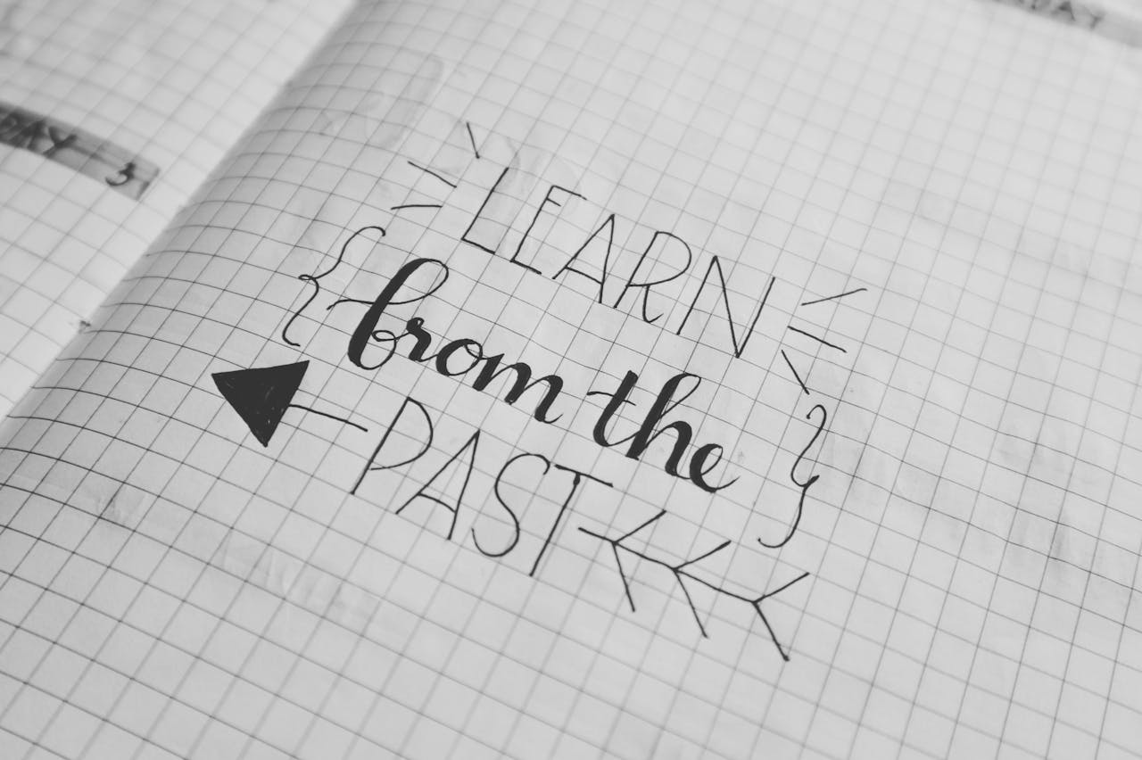 Black and white close-up of a handwritten motivational quote 'Learn from the Past' on graph notebook paper.